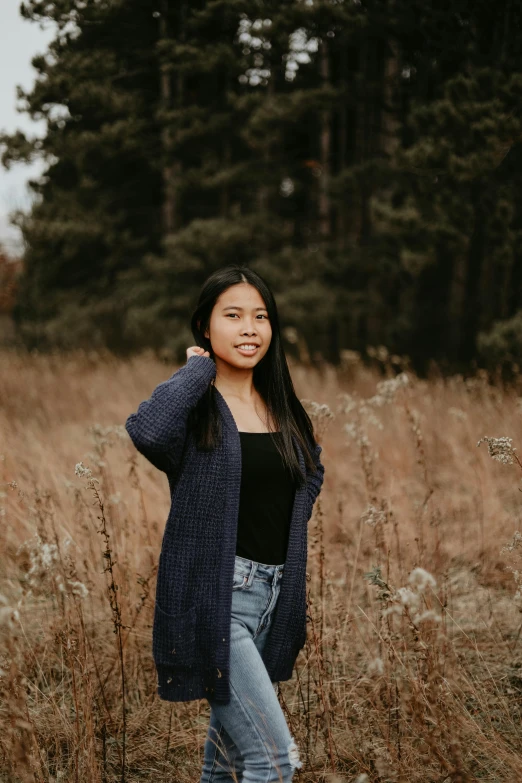 a woman standing in a field of tall grass, inspired by Ruth Jên, pexels contest winner, wearing a cardigan, young asian girl, college, near forest