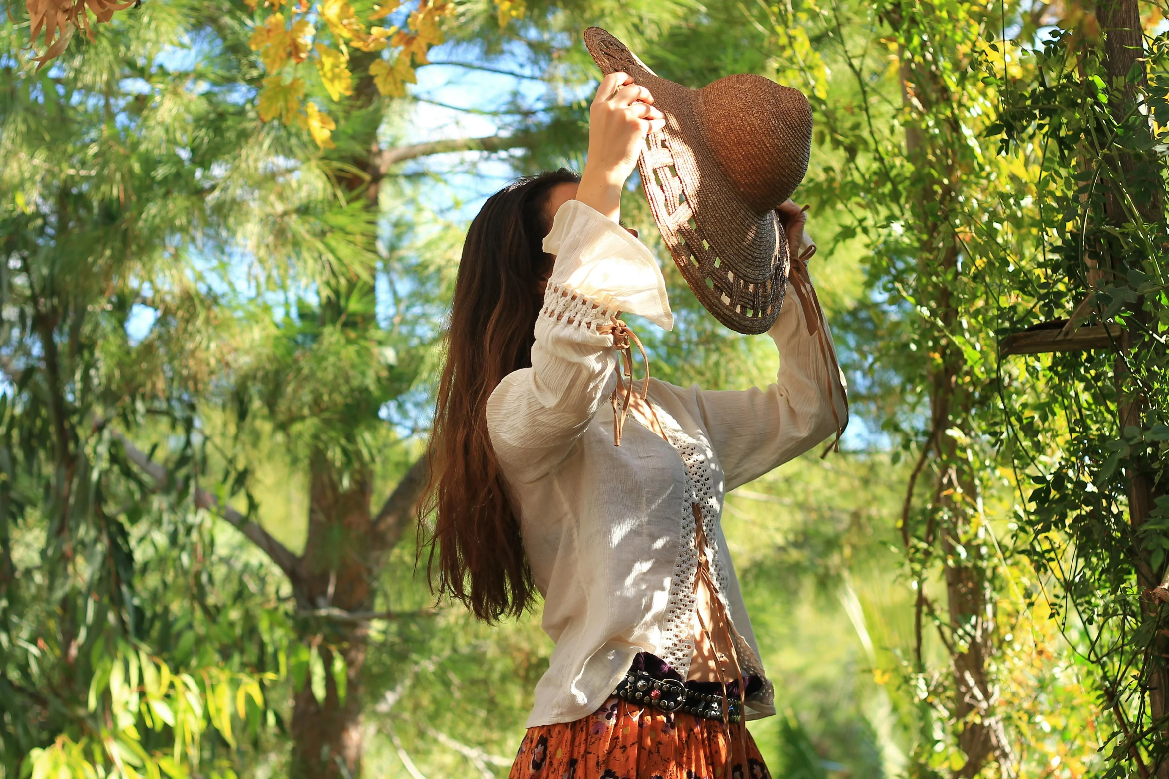 a woman holding a hat on top of her head, by Linda Sutton, pixabay contest winner, arabesque, soft autumn sunlight, cowgirl, loose - fitting blouses, foliage clothing