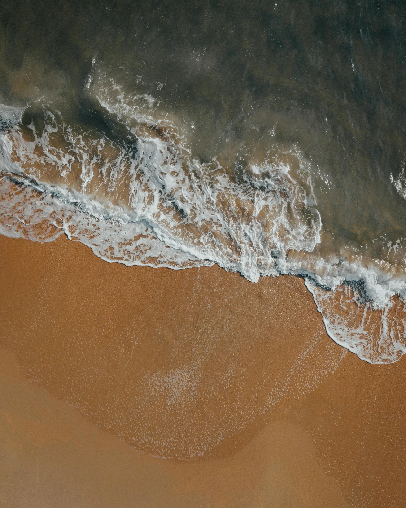 a person riding a surfboard on top of a sandy beach, from above, brown water, water flowing, trending photo