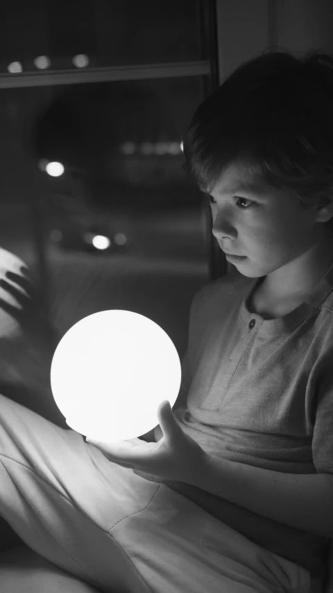 a black and white photo of a boy holding a light, magical realism, glowing sphere, using a magical tablet, tactile buttons and lights, a super-smart