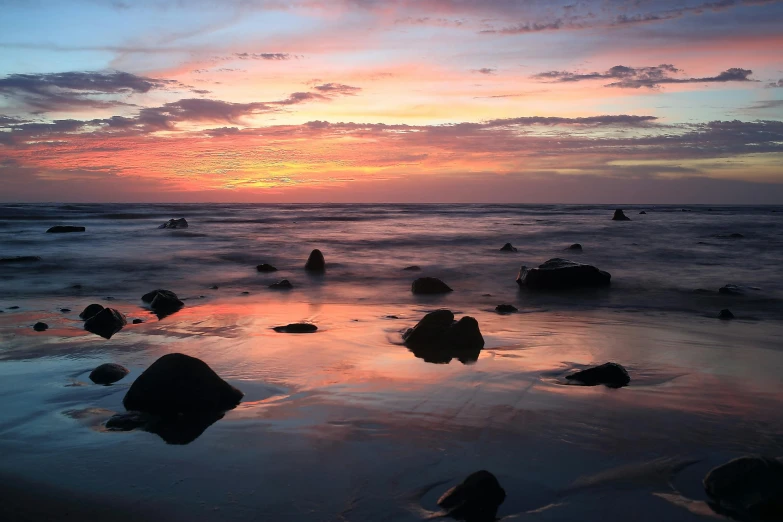 a group of rocks sitting on top of a sandy beach, during a sunset, body of water, an ocean, afar