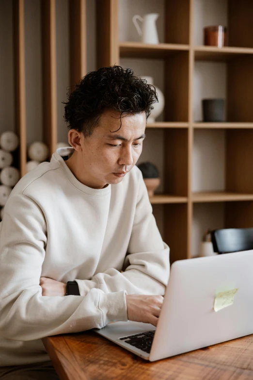 a man sitting at a table using a laptop computer, inspired by Fei Danxu, trending on pexels, wearing a white sweater, ethnicity : japanese, looking serious, maintenance