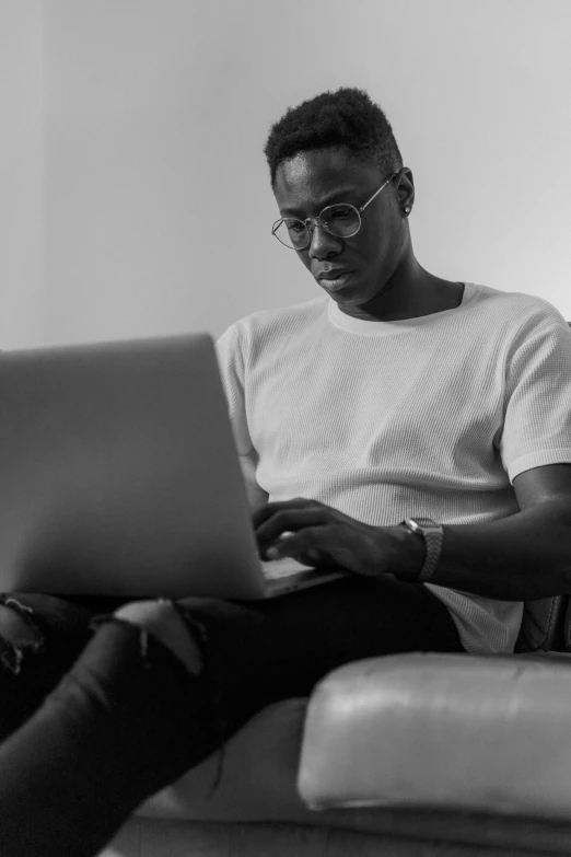 a man sitting on a couch using a laptop, a black and white photo, by Carey Morris, pexels, man is with black skin, typical cryptocurrency nerd, portrait of tall, julian ope