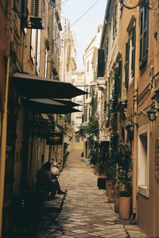 a person sitting on a bench in a narrow alley, inspired by Pietro da Cortona, unsplash contest winner, renaissance, awnings, seaside, 1999 photograph, scanned in