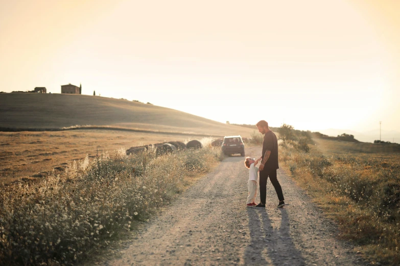 a woman and a child walking down a dirt road, pexels contest winner, renaissance, tuscany hills, cars and people, late summer evening, looking at the ground