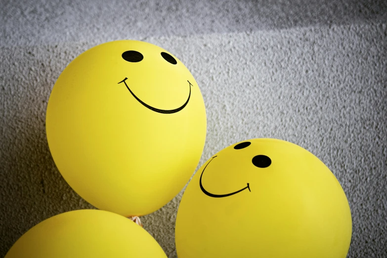 three yellow balloons with smiley faces on them, by Nina Hamnett, pexels, highly detailed photo of happy, colour photograph, on grey background, paul barson