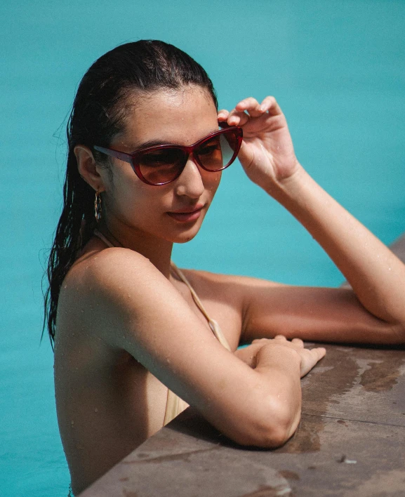 a woman sitting at the edge of a swimming pool, trending on unsplash, wear ray - ban glass, with brown skin, non binary model, gradient brown to red