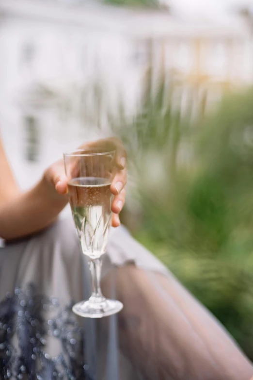 a woman sitting on a balcony holding a glass of wine, a picture, by Alice Mason, shutterstock, romanticism, delicate soft hazy lighting, champagne, waving, blur dreamy outdoor