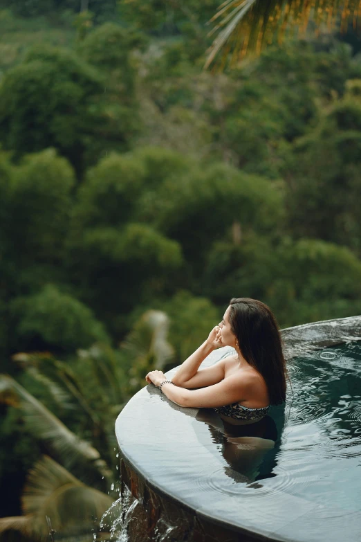 a woman sitting on the edge of a swimming pool, sumatraism, amidst of nature fully covered, curls, luxurious onsens, 2019 trending photo