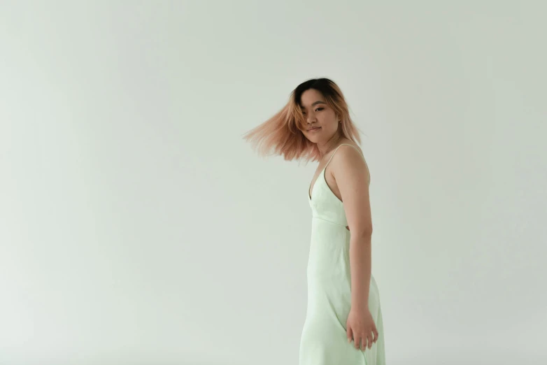 a woman in a green dress standing in front of a white wall, inspired by Russell Dongjun Lu, trending on pexels, hair waving in the wind, on a pale background, slight haze, half asian