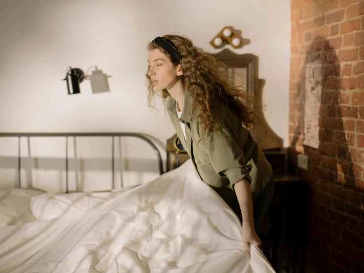 a woman standing next to a bed in a bedroom, pexels contest winner, happening, brown curly hair, flowing fabric, 6 : 3 0 am, performing