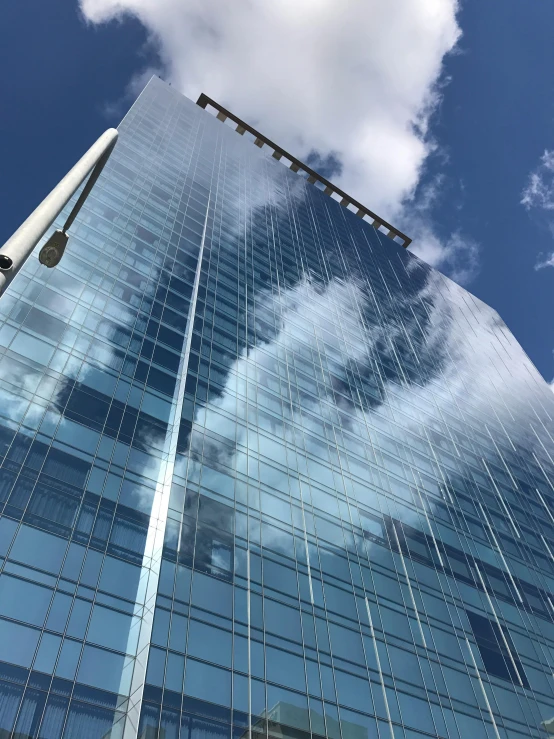 a tall glass building with a street light in front of it, face made out of clouds, photo taken in 2018, water coming out of windows, thumbnail