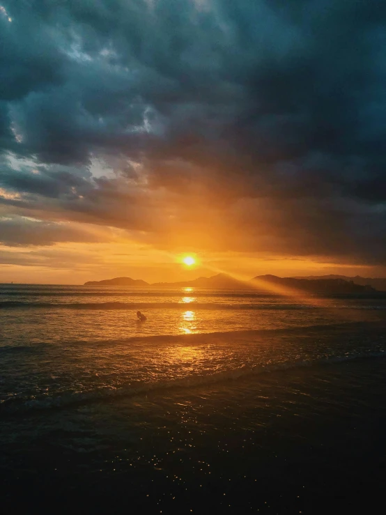 the sun is setting over the ocean on a cloudy day, unsplash contest winner, surfing, vibrant but dreary gold, low quality photo, center of image