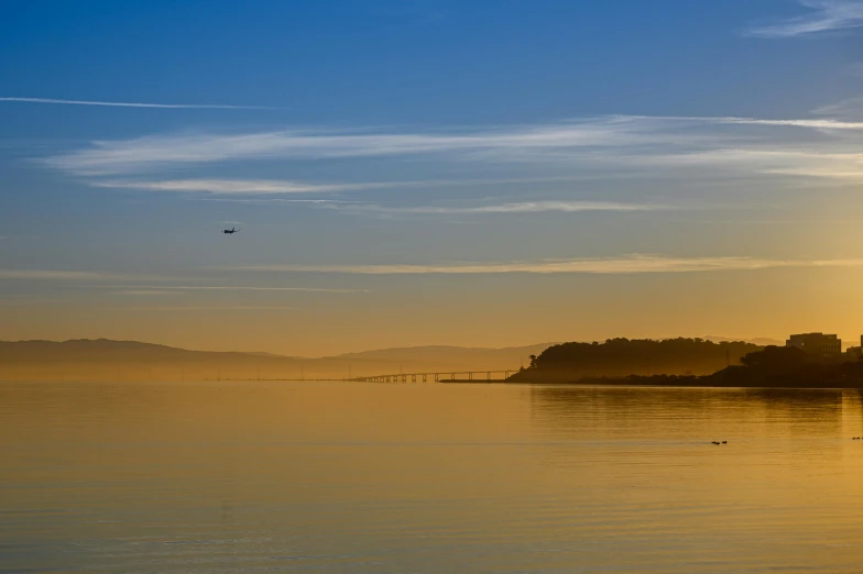 the sun is setting over a body of water, by Doug Ohlson, pexels contest winner, romanticism, yellow mist, holywood scene, flight, blue sky