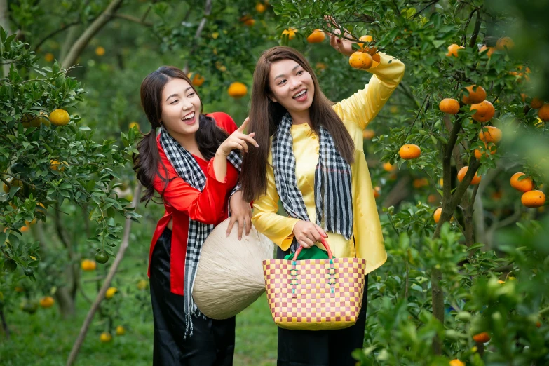 a couple of women standing next to each other, inspired by Tang Di, shutterstock, happening, garden with fruits on trees, square, vietnamese woman, black and orange