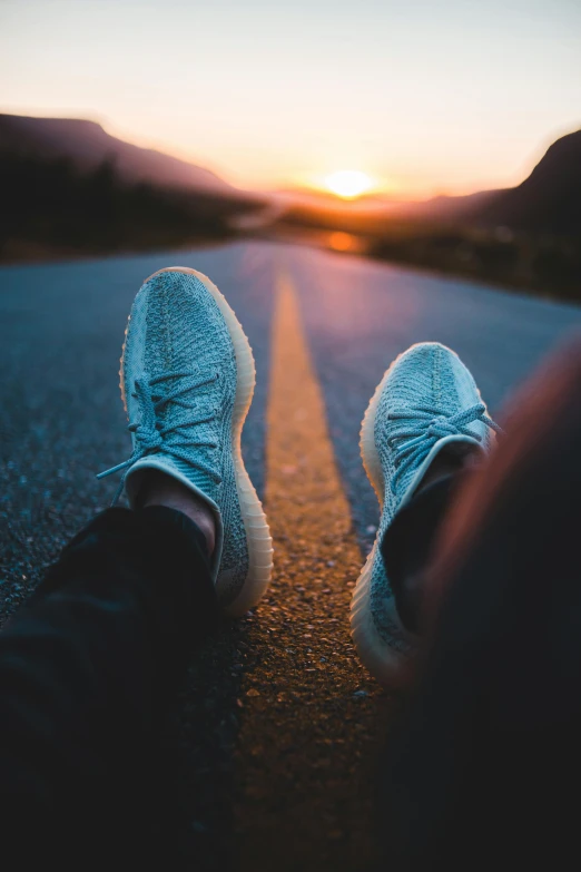 a person sitting on the side of a road at sunset, by Sebastian Spreng, pexels contest winner, running shoes, teal, rubber waffle outsole, looking straight