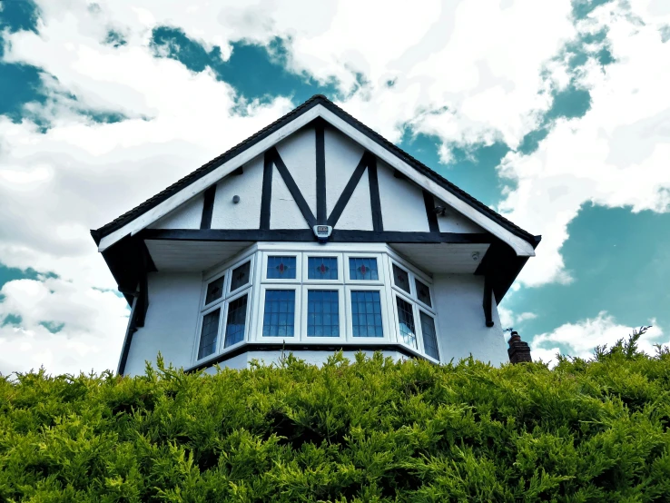 a white house sitting on top of a lush green hillside, by Joe Bowler, unsplash, arts and crafts movement, bay window, camera angle from below, black house, an estate agent listing photo