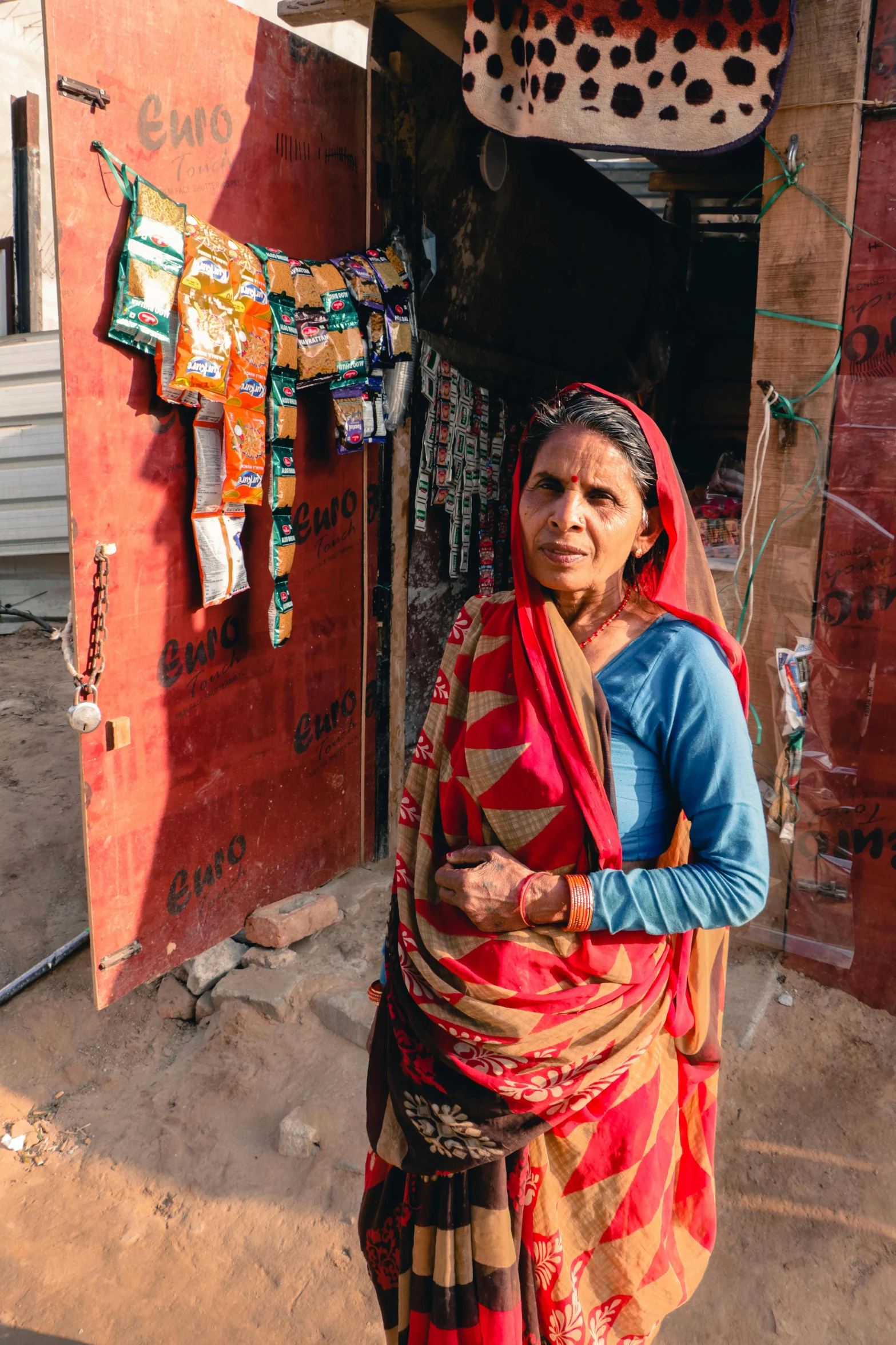 a woman standing in front of a red building, poverty, wearing a sari, at home, looking serious