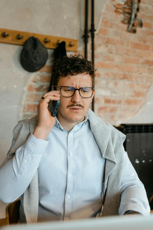 a man sitting at a table talking on a cell phone, trending on pexels, renaissance, handlebar mustache, non binary model, with glasses on, curly haired