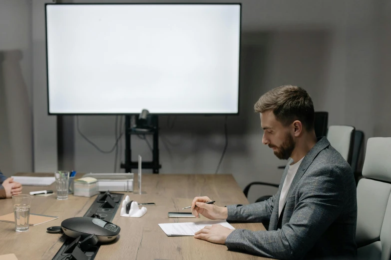 two men sitting at a table in front of a projector screen, by Adam Marczyński, pexels contest winner, in an call centre office, plain background, low quality footage, sitting behind desk