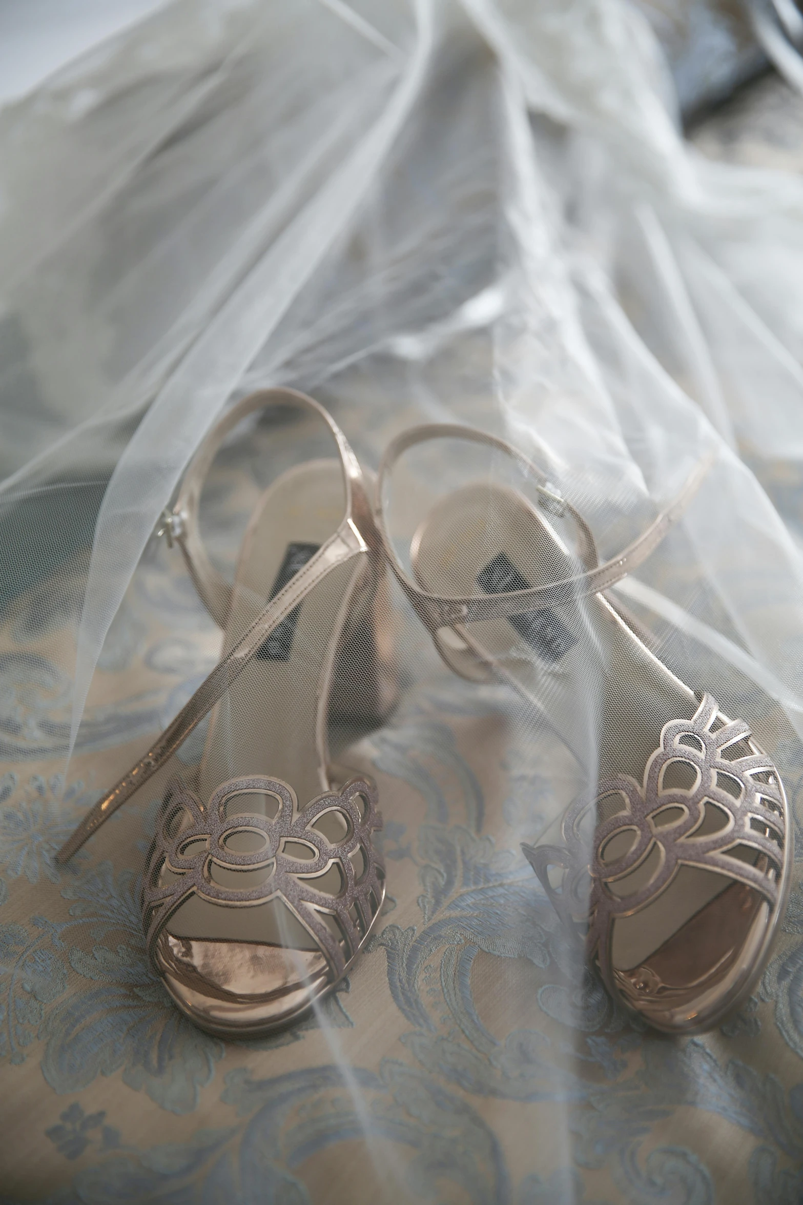 a pair of shoes sitting on top of a bed, veil, silver with gold accents, zoomed out view, straps