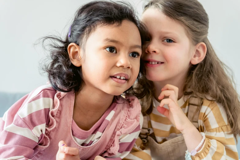 a couple of young girls sitting next to each other, by Ruth Simpson, trending on pexels, mixed race, closeup of an adorable, softplay, on grey background