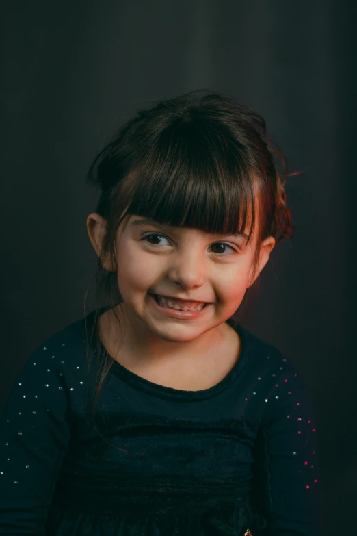 a little girl standing in front of a cake, dark grey backdrop studio, acting headshot, low lighting, smiling