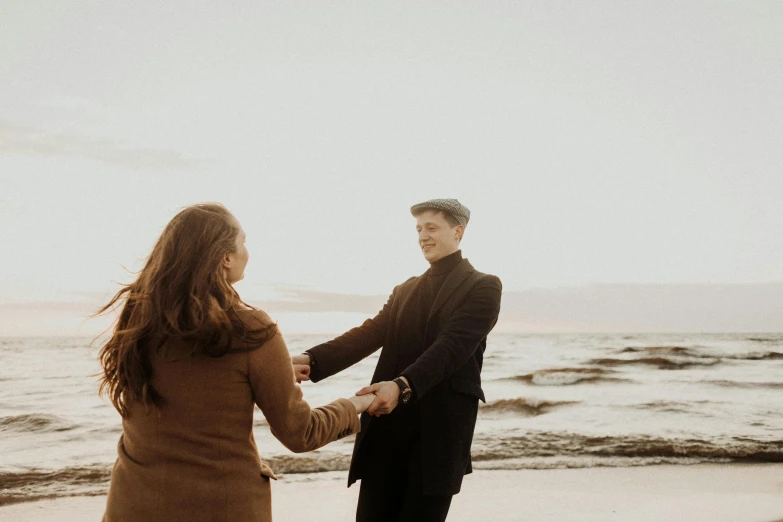 a man and a woman holding hands on a beach, an album cover, by Emma Andijewska, pexels contest winner, smiling at each other, brown, background image, low quality footage