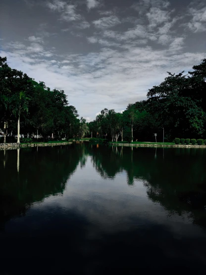 a body of water surrounded by trees under a cloudy sky, by Basuki Abdullah, city park, reflect photograph, cinematic image