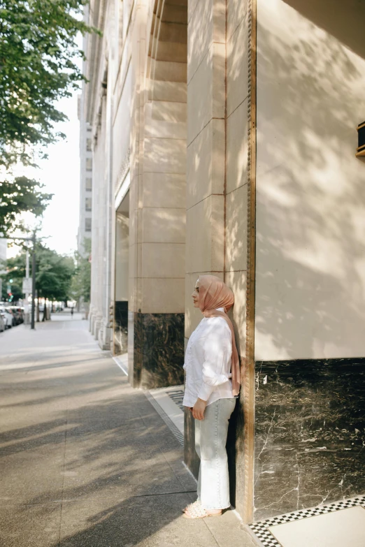 a man leaning against a pole in front of a building, a picture, trending on unsplash, white hijab, on madison avenue, woman's face looking off camera, wide full body