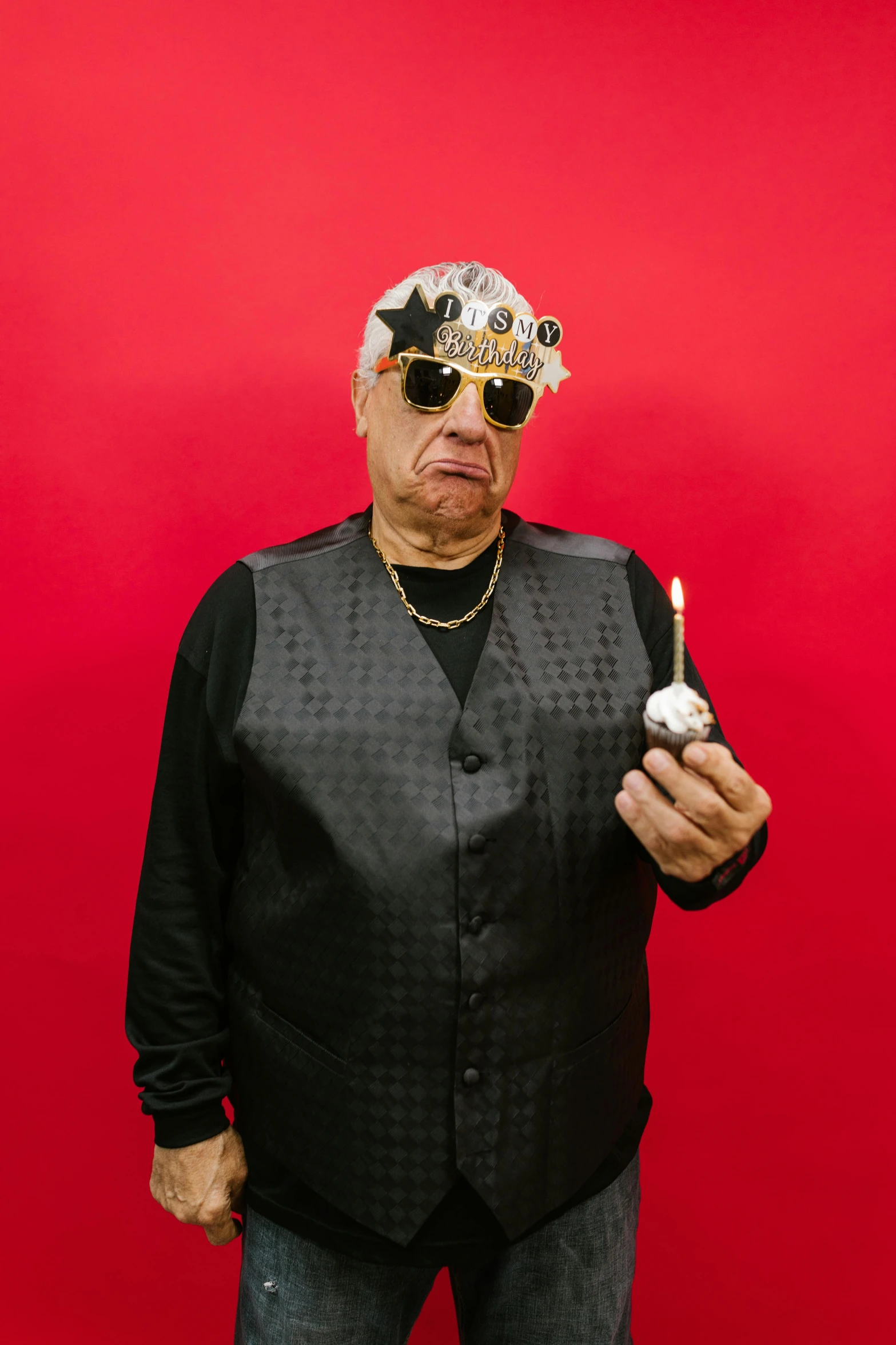 a man standing in front of a red wall holding a cigarette, wearing a party hat, wearing gold glasses, danny de vito, profile image