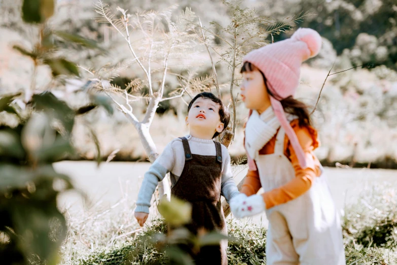 a couple of kids standing on top of a lush green field, pexels contest winner, 🍂 cute, beanie, blushing, li zixin