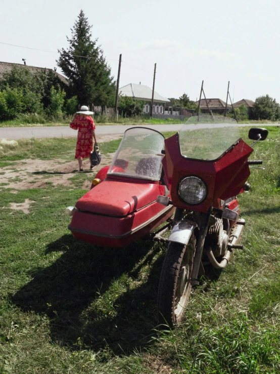 a red motorcycle parked on top of a lush green field, by Attila Meszlenyi, instagram, photorealism, soviet suburbs, old car, low quality photo, romanian