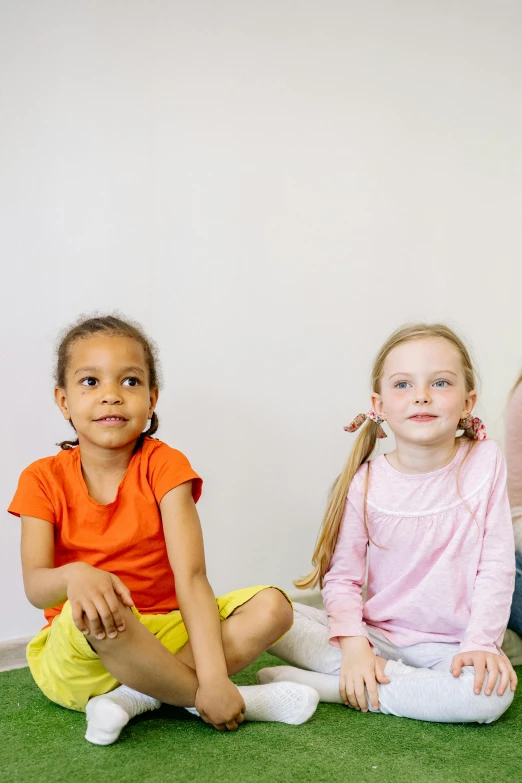 a group of children sitting on the floor next to each other, two girls, looking off to the side, promo image, slide show