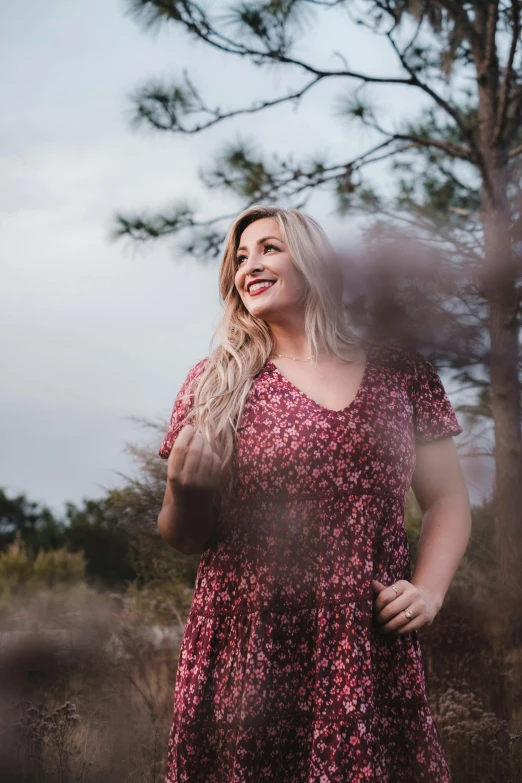 a woman standing in a field with trees in the background, unsplash, alluring plus sized model, a blond, concert photo, smiling and looking directly