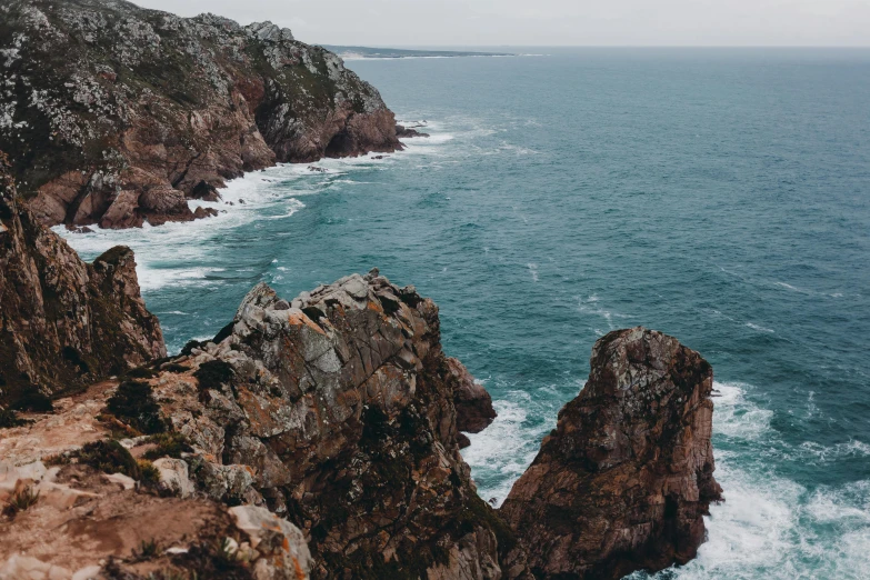 a person standing on top of a cliff next to the ocean, pexels contest winner, cornwall, rock arcs, thumbnail, brown