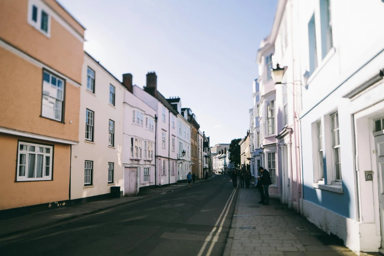 a couple of people that are walking down a street, by Rachel Reckitt, pexels contest winner, white houses, warwick saint, exterior view, warm coloured