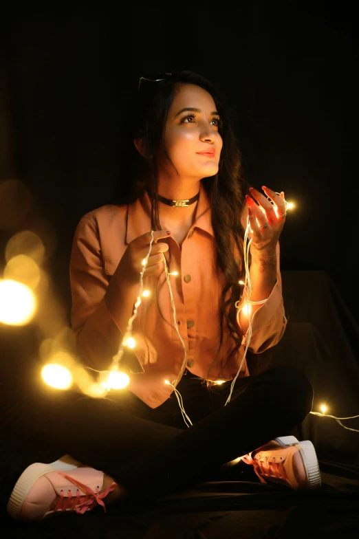 a woman sitting on a bed holding a string of lights, profile image