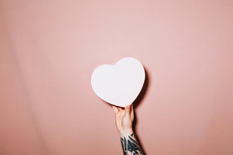 a person holding a paper heart in their hand, an album cover, inspired by Elsa Bleda, trending on pexels, smooth pink skin, tattoo, plain background, aww