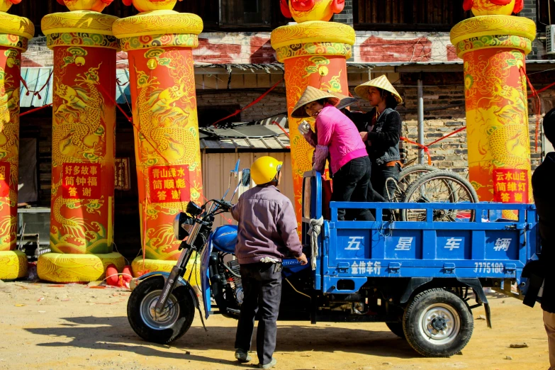 a group of people riding on the back of a truck, inspired by Sheng Maoye, yellow and blue color scheme, large pillars, motorbike, chinese village