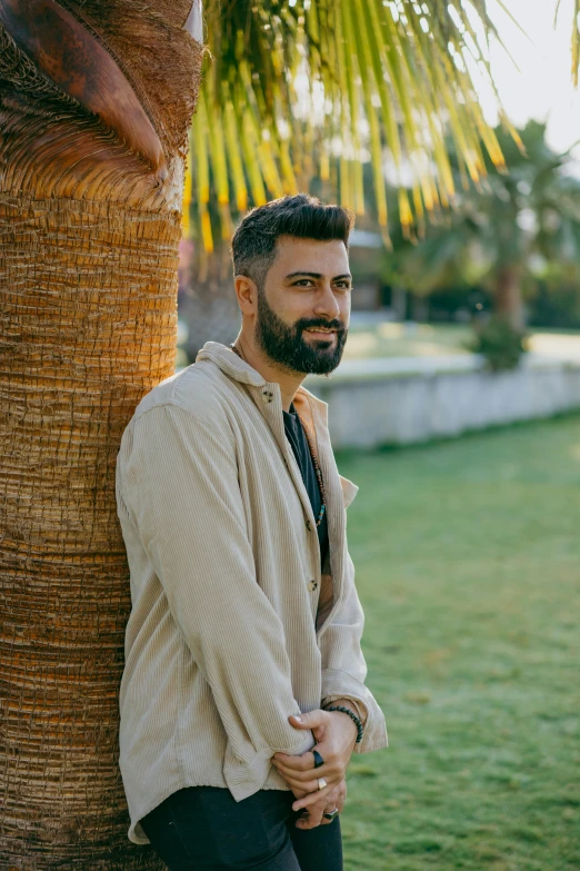 a man standing next to a palm tree, an album cover, by Ismail Acar, wearing a linen shirt, profile image, outdoor photo, a portrait of rahul kohli