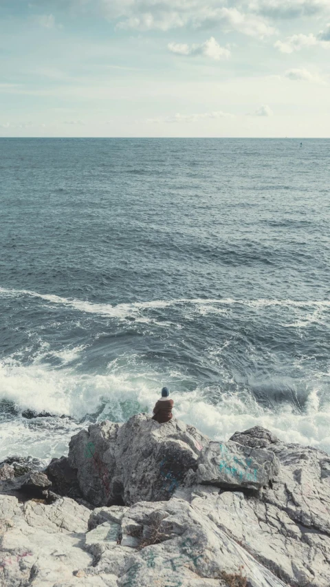 a person sitting on top of a rock next to the ocean, by Elsa Bleda, pexels, happening, sea waves, low quality photo, sittin