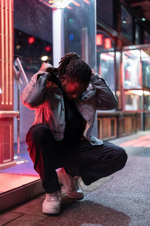 a man squatting on the sidewalk in front of a store, an album cover, trending on pexels, hero pose colorful city lighting, depressed dramatic bicep pose, chief keef, concert