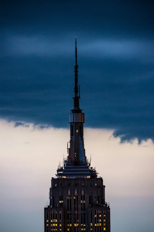 the empire state building is lit up at night, an album cover, by Sven Erixson, unsplash, on a cloudy day, evening light, spire, telephoto