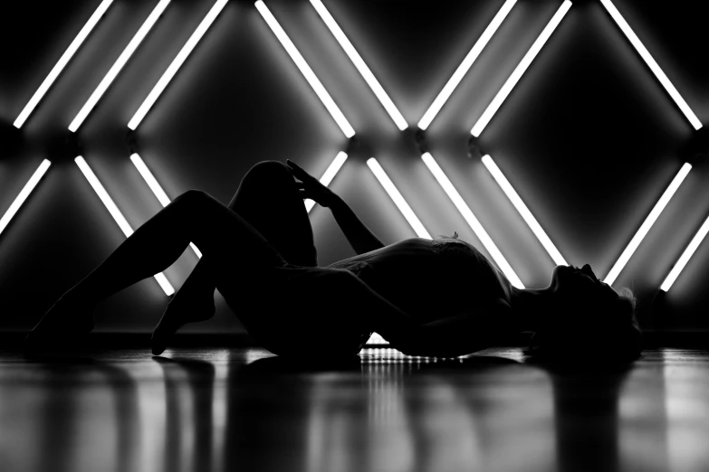 a black and white photo of a woman laying on the floor, by Julia Pishtar, light and space, neon background lighting, beautiful female body silhouette, geometric backdrop; led, concept photoset