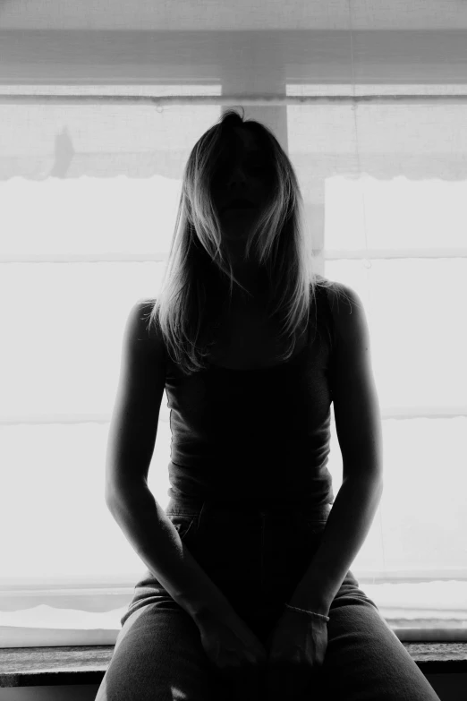 a black and white photo of a woman sitting in front of a window, flickr, difraction from back light, a girl with blonde hair, silhouette :7, teenage