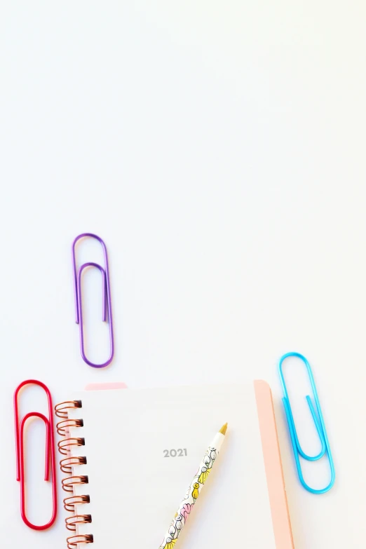 a notebook sitting on top of a table next to a pair of paper clips, trending on pexels, white background, colorful medical equipment, taken on iphone 14 pro, wallpaperflare