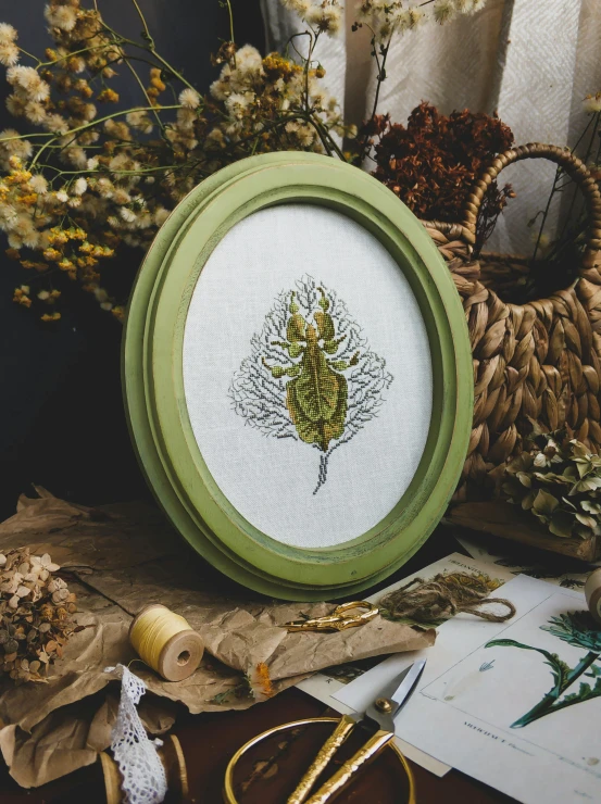 a picture frame sitting on top of a table next to a bunch of flowers, a cross stitch, inspired by Master of the Embroidered Foliage, featured on behance, plume of seaweed, crustacean, olive green, yulia nevskaya