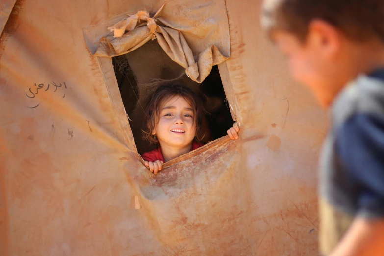 a boy and a girl looking out of a window, by Jessie Algie, pexels contest winner, hurufiyya, cardboard tunnels, portrait of bedouin d&d, smiling girl, tent