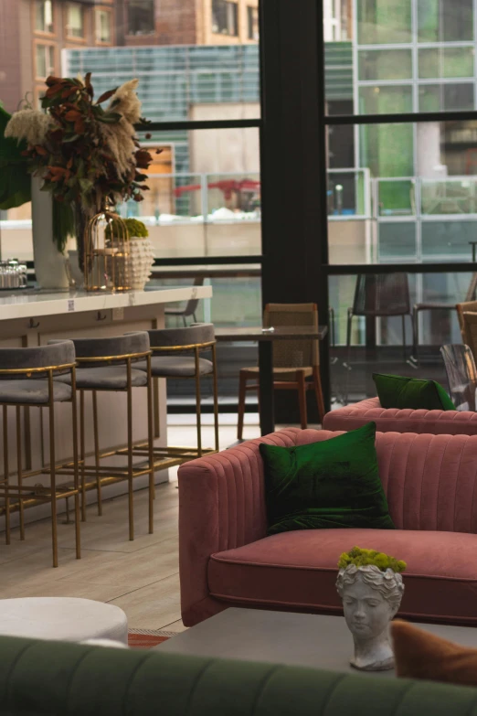 a woman sitting on a couch in a living room, bar in background, green magenta and gold, city rooftop, plush furnishings